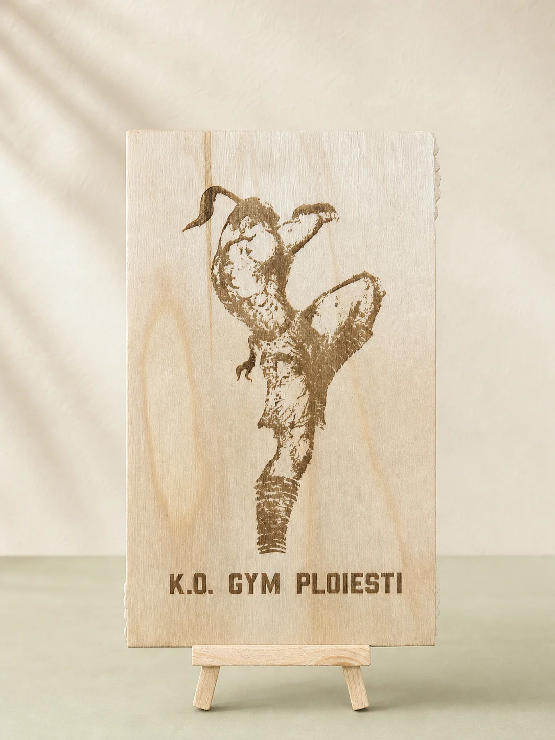 Placă verticală din lemn gravată cu un sportiv și textul K.O. Gym Ploiești, pe șevalet