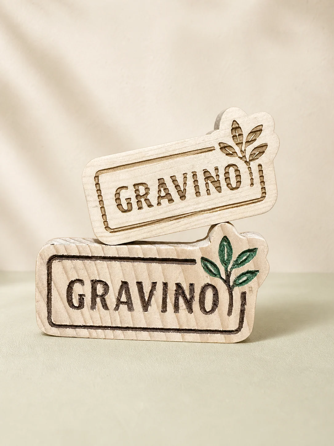 Două plăcuțe din lemn gravate cu logoul Gravino și elemente vegetale